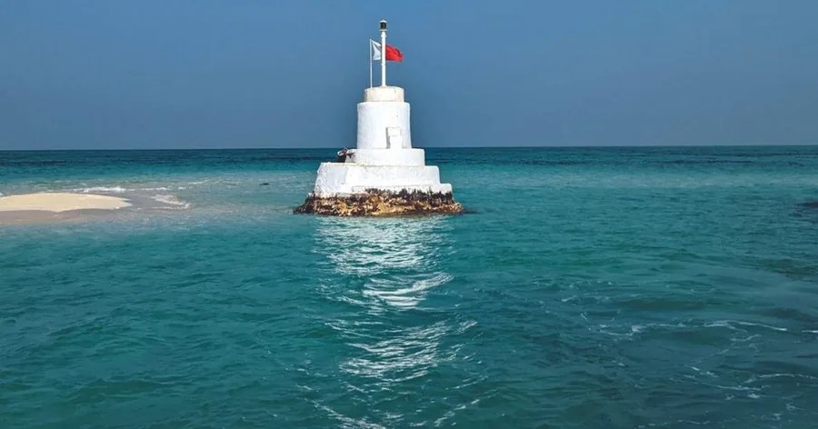 Ein kleiner weißer Leuchtturm auf einem Riff im türkisfarbenen Wasser vor Bahrain